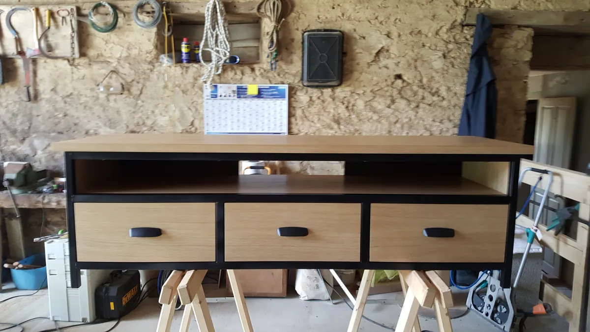 Un meuble à trois tiroirs en bois et noir, sur des tréteaux à l’atelier