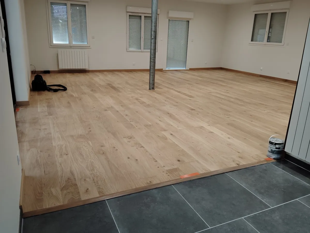 Parquet en bois clair posé jusqu’à un carrelage sombre, avec un seuil